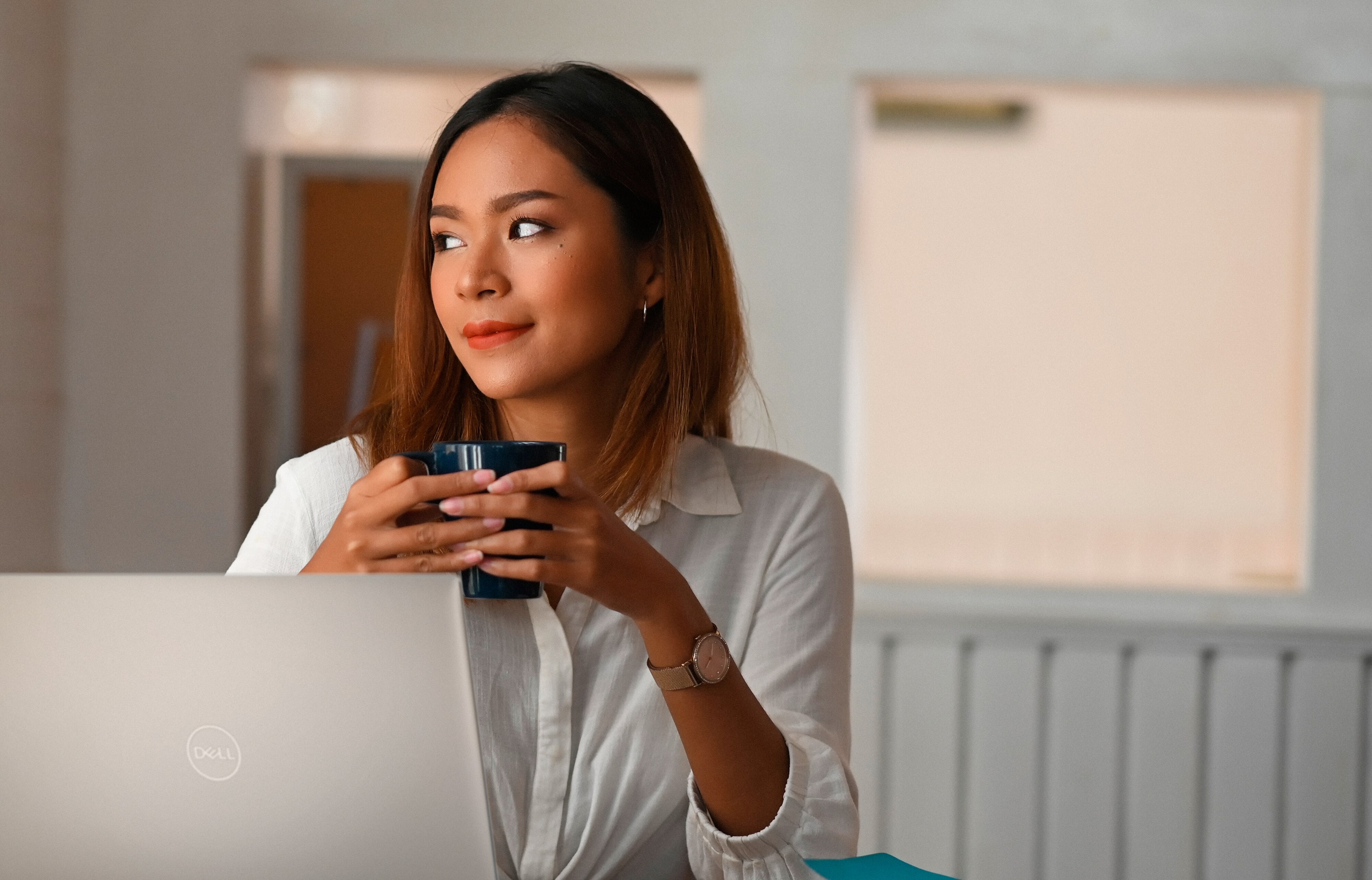 Femme tenant une tasse et utilisant un ordinateur portable Dell posé sur une table devant elle.