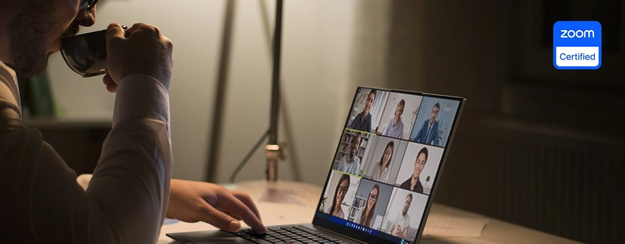 A person sits at a table with the Lenovo ThinkPad X1 Carbon Gen 11 laptop participating in a Zoom conference call.