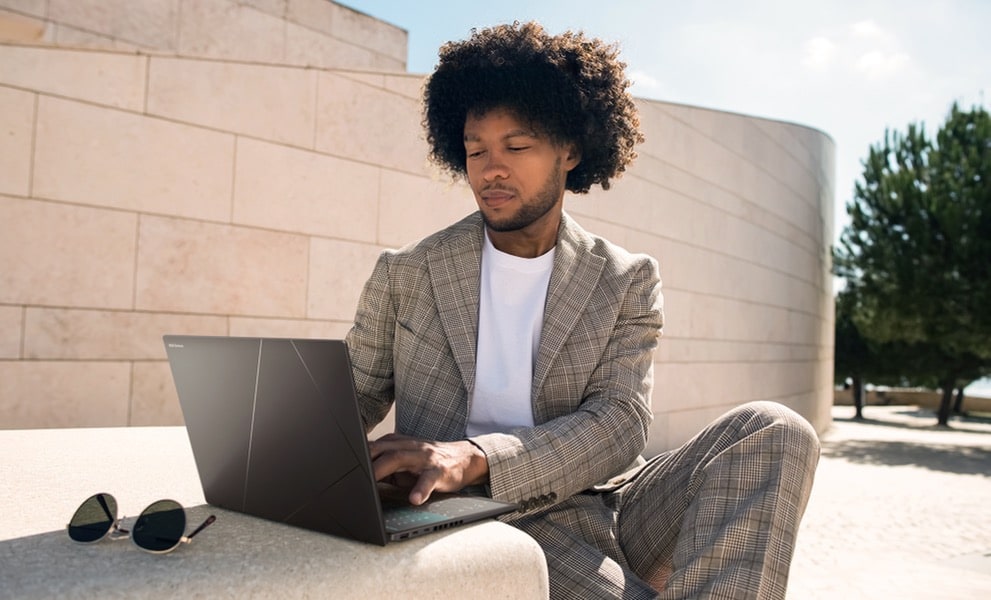 Un homme portant un costume beige assis sur les escaliers utilisant un Zenbook 14 OLED ponder blue